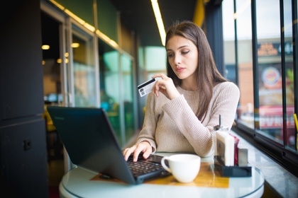 Woman in a cafe, holding a credit card and looking at her laptop