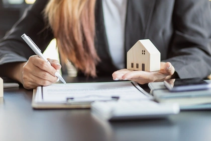 Woman holding toy house and writing in a pad