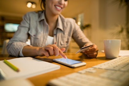 Woman holding her credit card and checking her phone at a desk