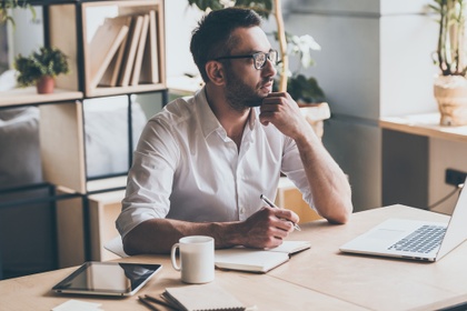 Man thinking while writing something down in a notebook
