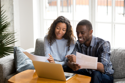 Happy couple looking at laptop and holding documents