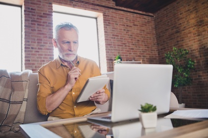 man thinking and making notes at laptop
