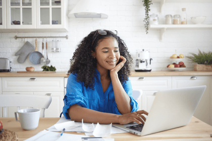 Smiling woman sat in the kitchen on her laptop