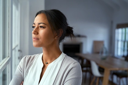 Young woman stands looking out a window at home.