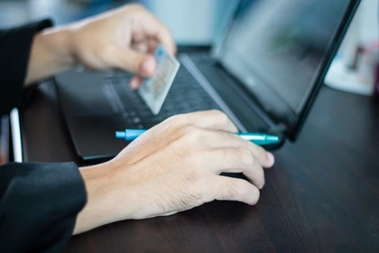 close up of a mans hands using a laptop, holding a credit card and a pen