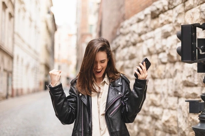woman making the winner gesture while holding her mobile phone