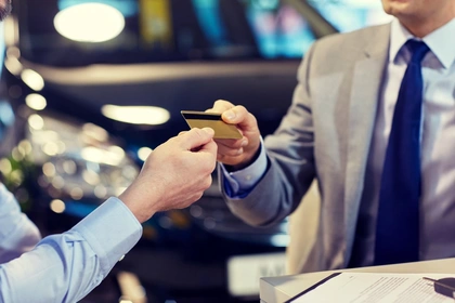 Business man handing a credit card over with a car in the background