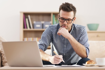 Man thinking while holding a pen in front of a laptop