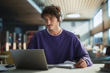 student in the library looking at his laptop with headphones on