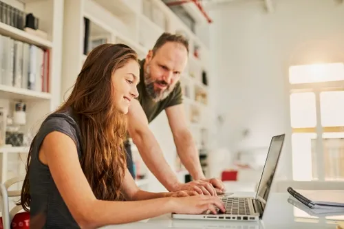 Dad and daughter both smiling and looking at their shared laptop screen.
