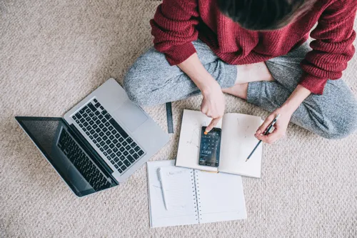 Woman sat on bedroom floor with laptop, calculator and documents