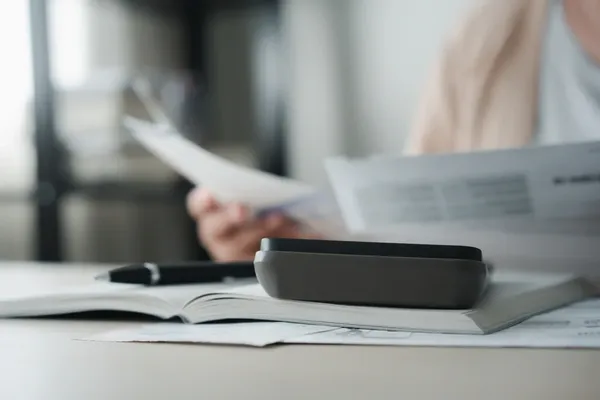 Close up image of someone looking through documents with a pen and calculator