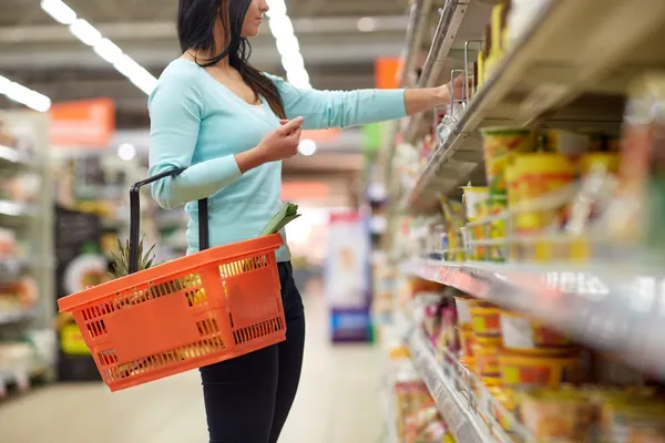 woman in supermarket holding a shopping basket and looking for cheap food items