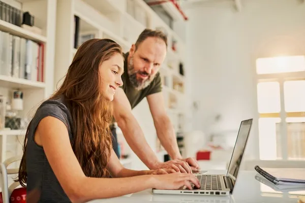 Dad and daughter both smiling and looking at their shared laptop screen.