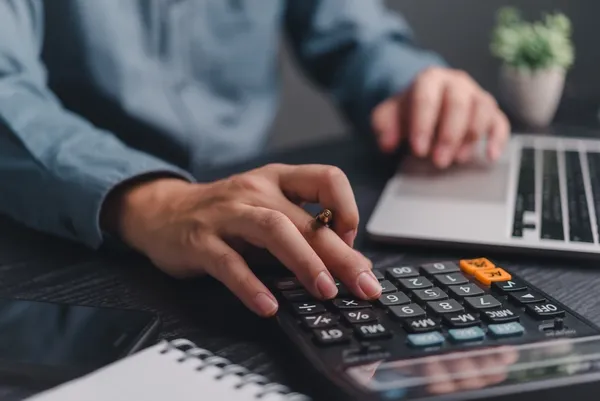close up of a man on his laptop and using a calculator