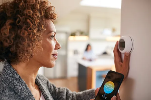 A lady with dark curly hair adjusts her thermostat