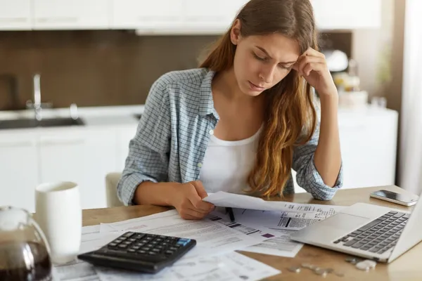 Woman sat at the table with her laptop and surrounded by paperwork, calculating debts