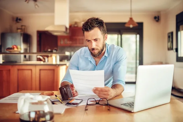 Man sat at the table looking through documents with his wallet and laptop open