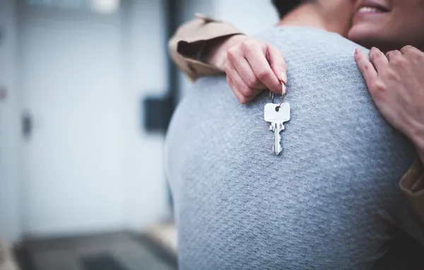 Couple hugging holding house keys. Their front door is in the background