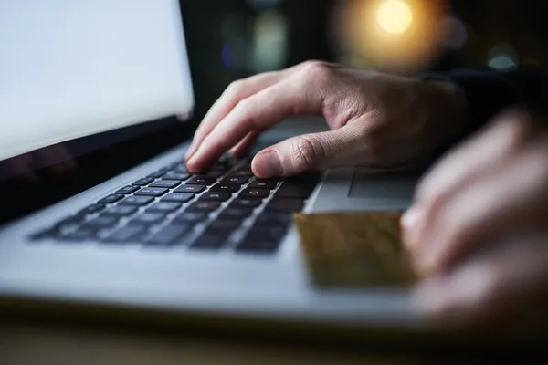 zoomed in on a man using a laptop with a credit card in his hand.