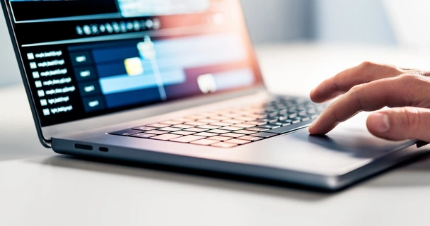 A hand touches the trackpad of a laptop. Editing software is on the screen.