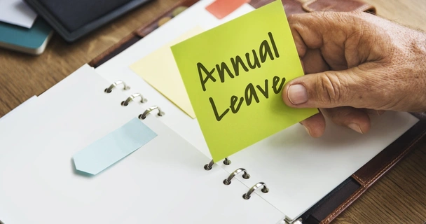 Open diary with hand holding a sticky note labelled annual leave
