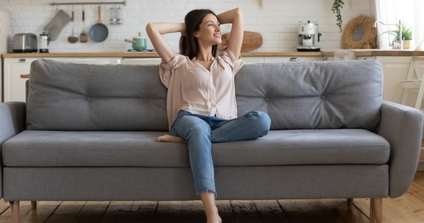 Happy single lady in peach top and jeans sitting on a grey sofa