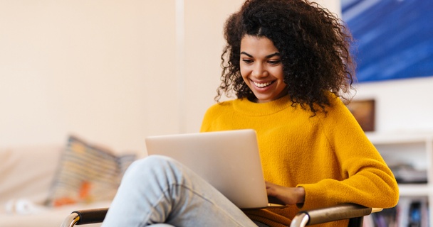 Lady with curly hair in yellow jumper smiling while using a laptop