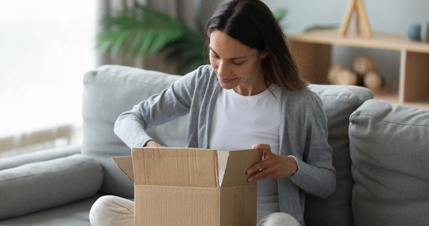 Happy young Caucasian woman sit on couch in living room unpack cardboard box with Internet order