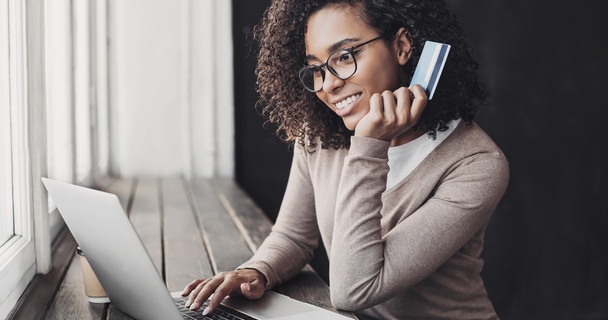 Happy woman holding payment card using a laptop