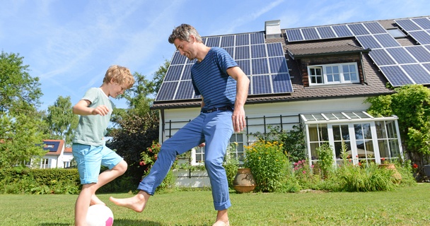 son and father playing in front of solar panel house