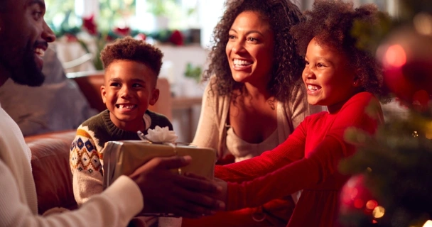 Warmly lit, smiling family exchanging Christmas gifts
