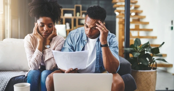 worried couple sat at a table looking at their laptop and paperwork