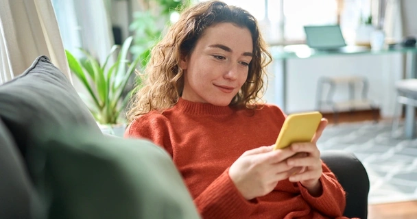 Happy young woman in red jumper using yellow phone