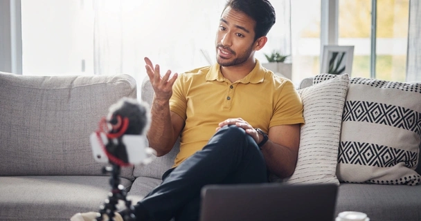 content creator sat on the sofa creating a video with his smartphone