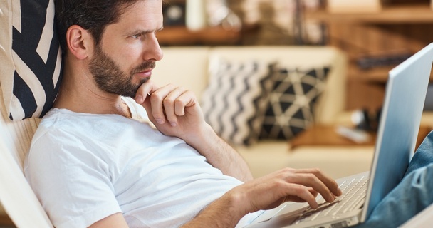 Thoughtful looking white man in t-shirt using laptop