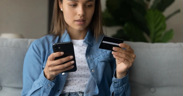 Woman looking at a credit card while holding a smartphone