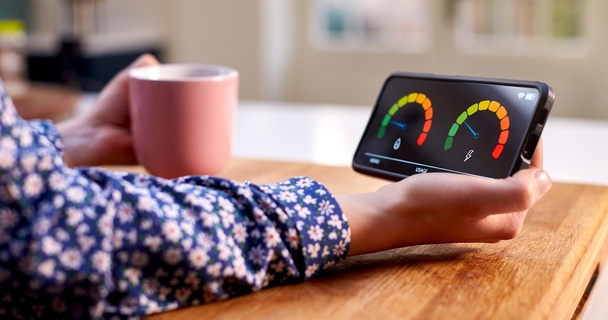 Lady in blue floral blouse holding pink mug and smart meter with two dials