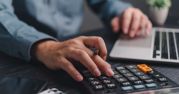 close up of a man on his laptop and using a calculator