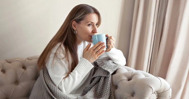 Woman sat on the sofa under a blanket drinking a hot drink
