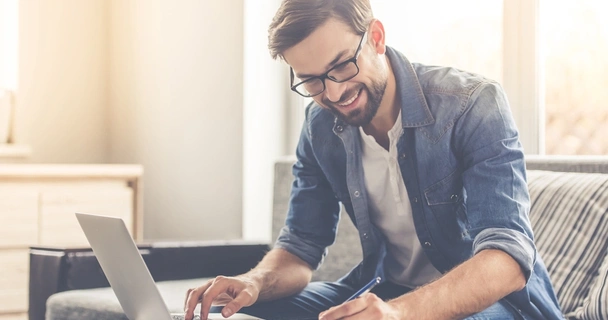 man on laptop smiling and making notes