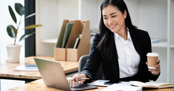 business woman holding a drink and working on her laptop