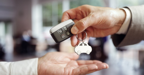 One person hands a car key to someone else. Only their hands and the car key fob are visible.