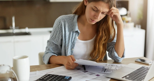 Woman sat at the table with her laptop and surrounded by paperwork, calculating debts