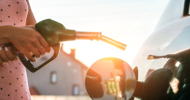 Lady in pink spotted dress refuelling her car at sunset