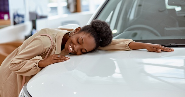 Happy lady hugging her new white car in the dealership