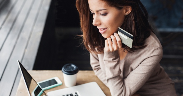 Young woman on her laptop in a coffee shop holding a credit card