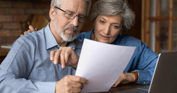 Older couple looking over a document with their laptop open