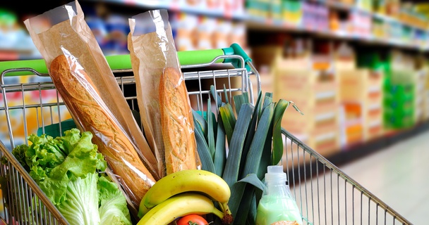 supermarket trolley with green handle filled with groceries including bananas, bread and greens