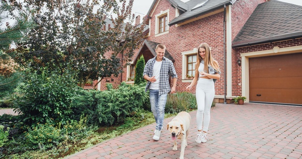 Young couple walking labrador dog outside red brick house